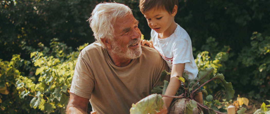mature man holding plants from a garden up to a young boy