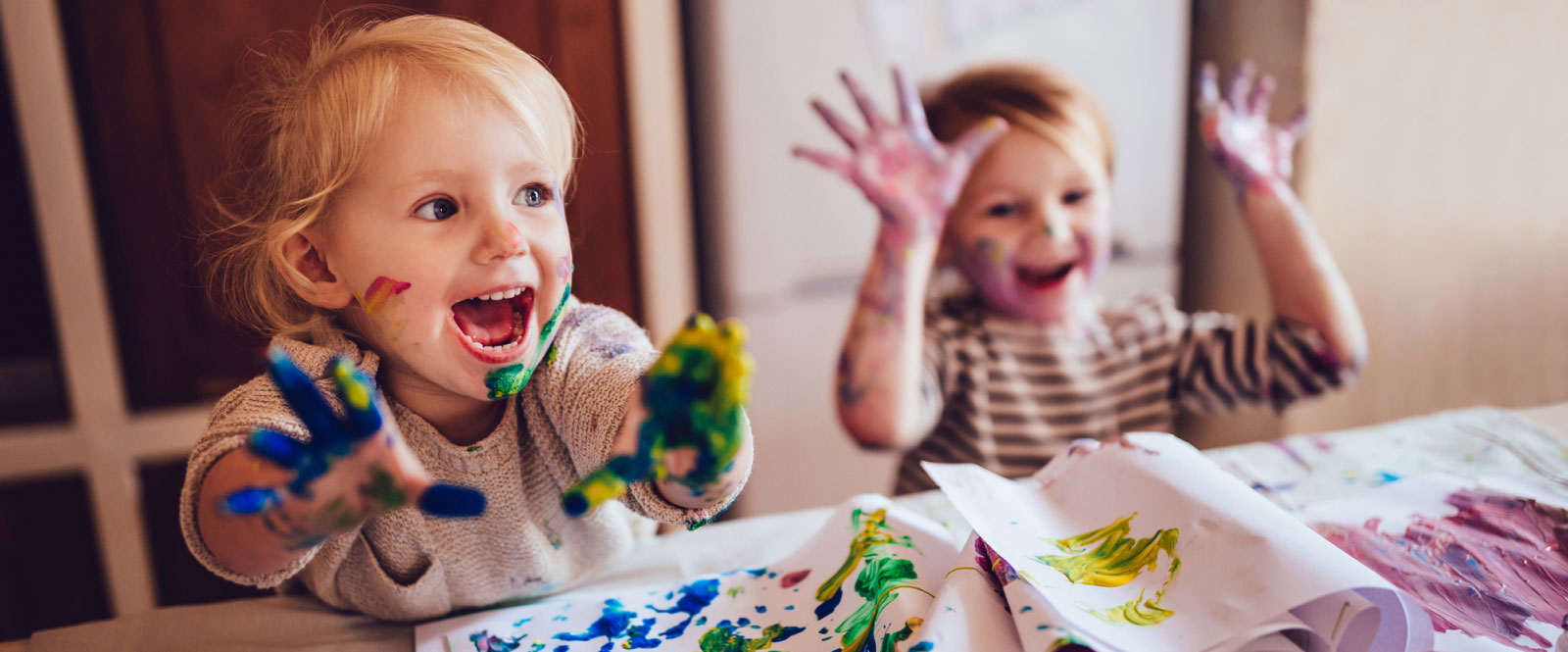 two todderls finger painting with paint on their hands and faces