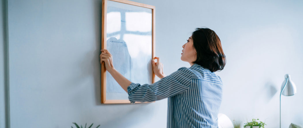 woman hanging a framed picture on a wall